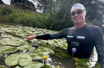 Andreas Fath steht im Neoprenanzug zwischen Seerosen